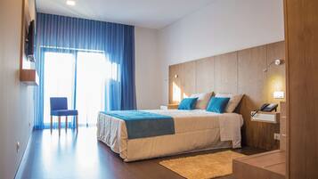 A modern hotel room with a large bed, a chair, a desk with a phone, and a window with curtains.