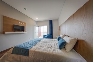 A modern hotel room with a large bed, a mounted TV, a balcony with a chair, and a wooden headboard. - Belmonte Sinai Hotel (Belmonte)