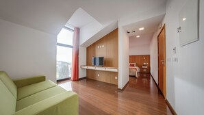 A modern living room with a sofa, a TV, wooden cabinets, and a kitchen area in the background. - Belmonte Sinai Hotel (Belmonte)
