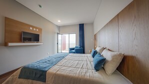 A modern hotel room with a large bed, a mounted TV, a balcony with a chair, and a wooden headboard. - Belmonte Sinai Hotel (Belmonte)
