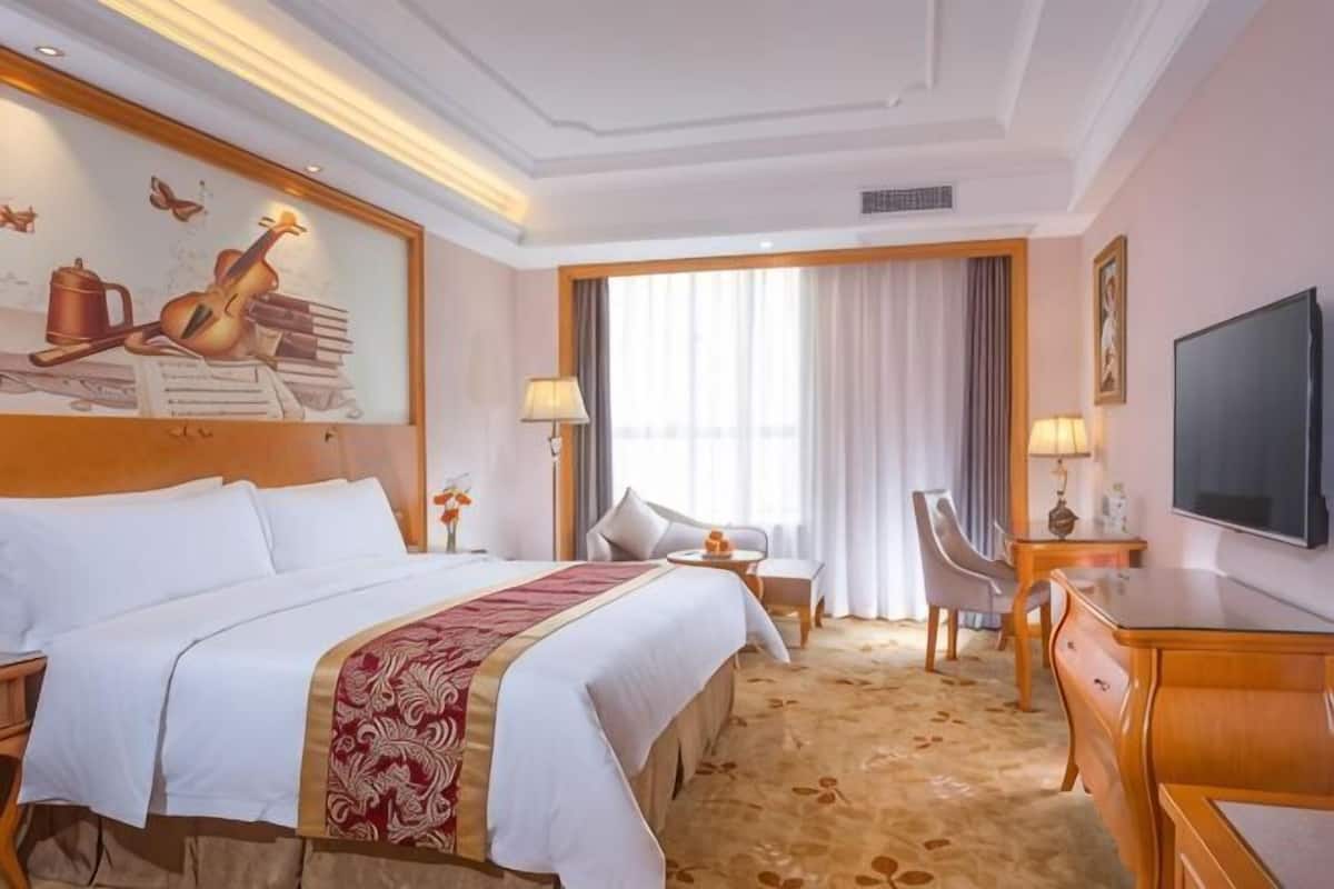 Une chambre dâhĂŽtel avec un grand lit, un bureau, une chaise, une tĂ©lĂ©vision et un tableau au mur.