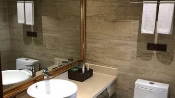 A bathroom with a large mirror, a sink, a toilet, and towels on the wall.