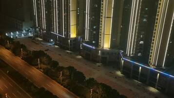Een nachtzicht van een modern hoog gebouw met verlichte verticale lijnen en een goed verlicht parkeerterrein.