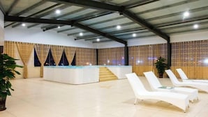 A spacious indoor area with a pool, white lounge chairs, and a staircase leading to a higher level. - Venus Royal Hotel (Guilin Airport) (Guilin)