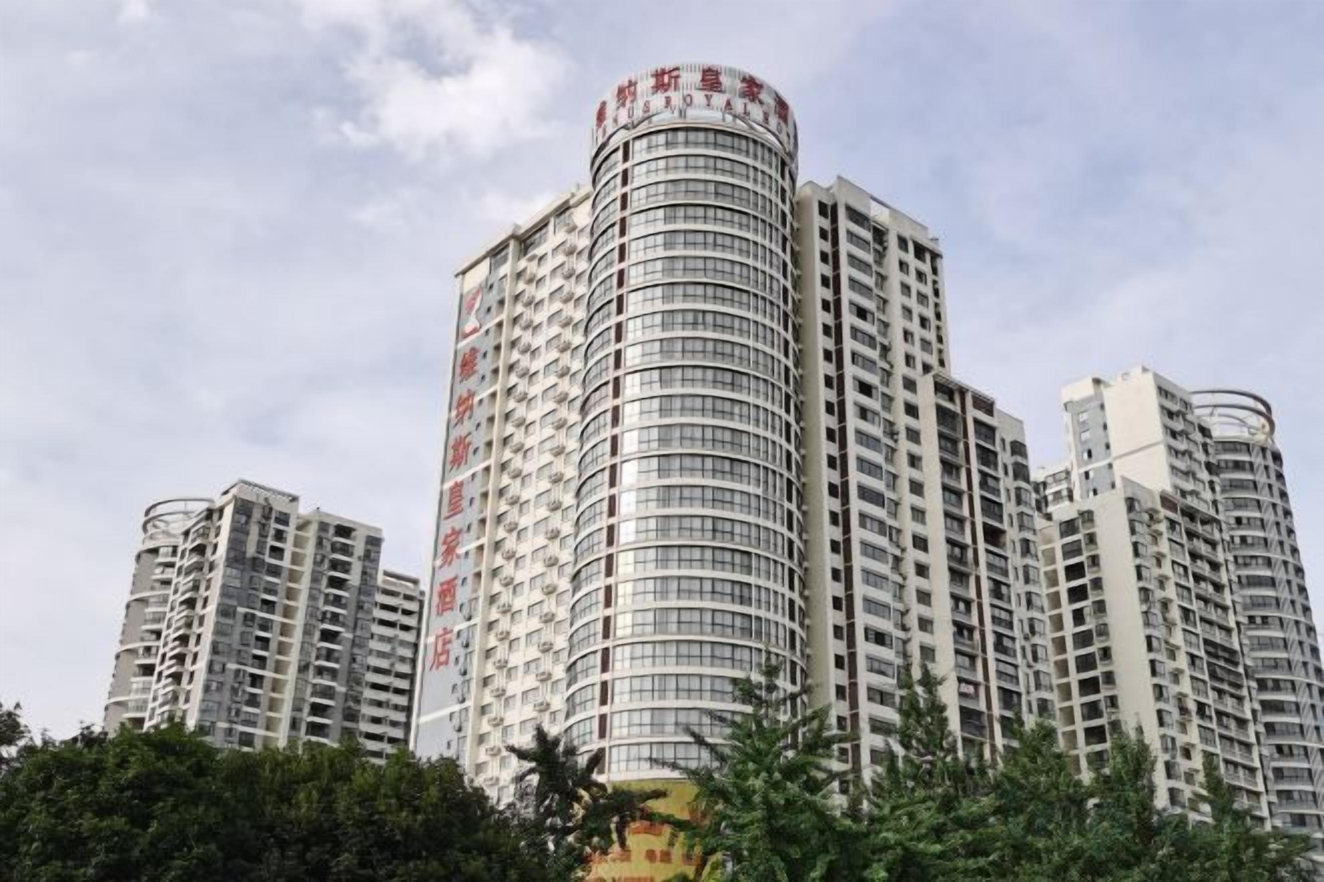 A high-rise building with multiple floors and balconies, surrounded by trees.