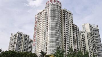 A high-rise building with multiple floors and balconies, surrounded by trees.