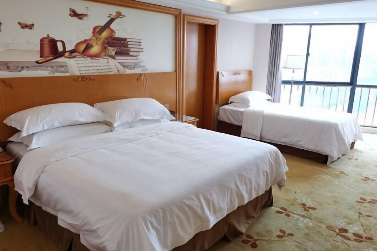 A hotel room with two beds, a large window with a view, and a wall with a musical instrument and books.