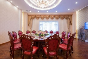 A conference room with a round table, red upholstered chairs, a chandelier, and a television on the wall.