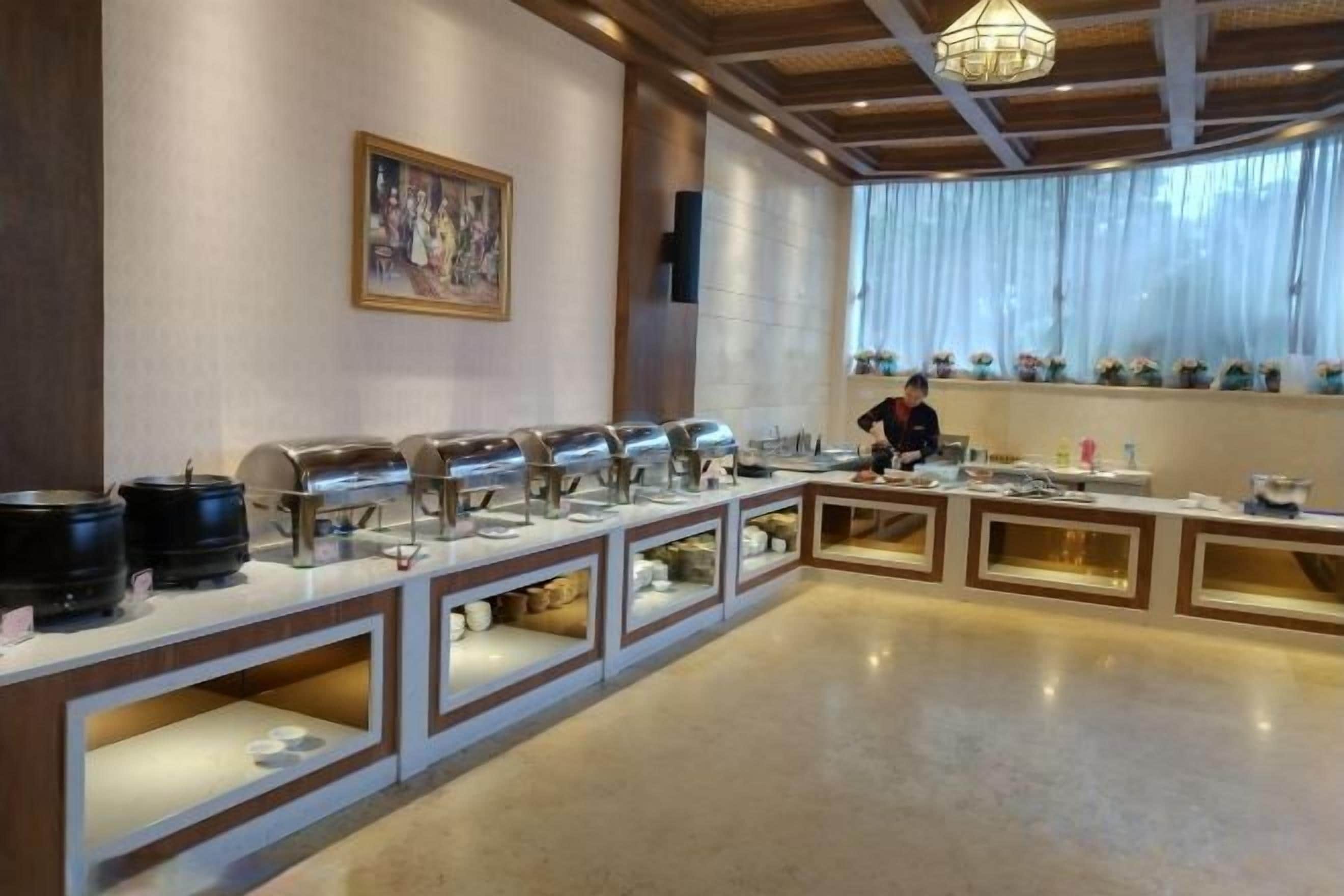 A buffet setup with multiple serving stations, a person in the background, and a large window with curtains.