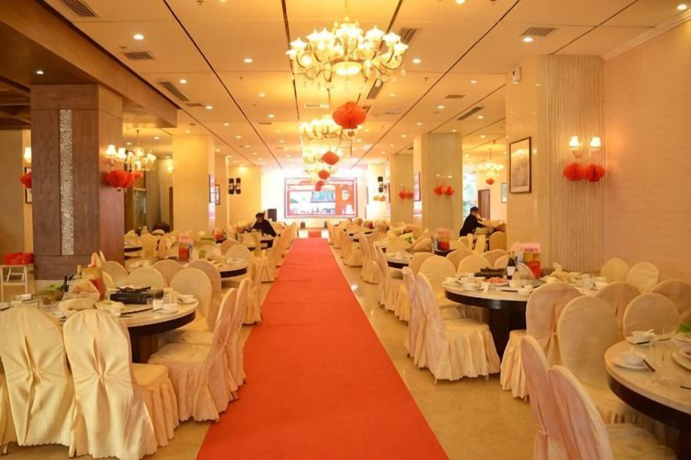 Un salón de banquetes con mesas y sillas redondas, una alfombra roja y candelabros.