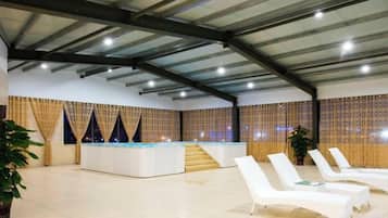 A spacious indoor area with a reception desk, a staircase, and several white lounge chairs.