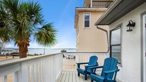Een balkon met twee blauwe Adirondack-stoelen, een palmboom en uitzicht op het strand en de oceaan.