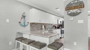 Een moderne keuken met witte kasten, een granieten aanrechtblad en een grote klok aan de muur.