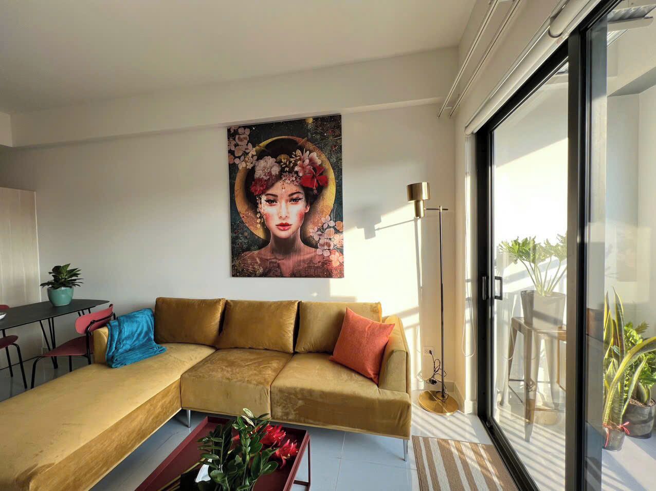 A modern living room with a sectional sofa, a coffee table with flowers, a dining area with a table and chairs, and a large window with a view of the outdoors.