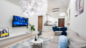 Ein modernes Wohnzimmer mit Fernseher, einem weißen Sofa, einem Couchtisch und einem Essbereich mit blauen Stühlen.