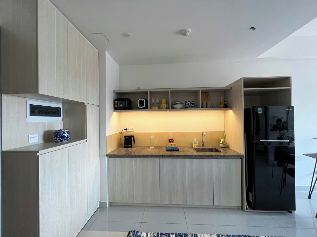 Una cocina moderna con alacenas de madera clara, encimera de granito, refrigerador negro y horno empotrado.