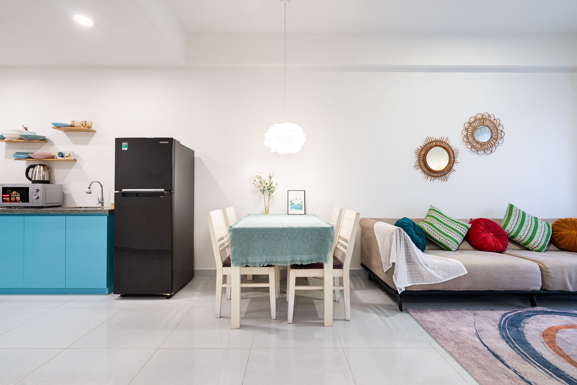 A modern kitchen with a black refrigerator, a dining table with chairs, a sofa with colorful cushions, and decorative wall art.