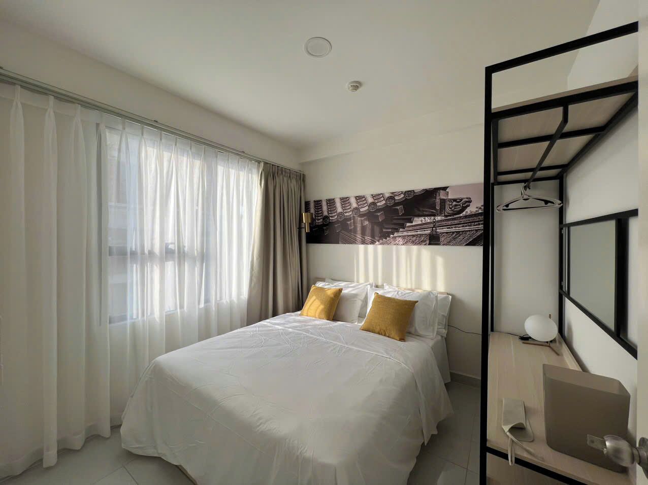 Una habitación de hotel moderna con una cama grande, un escritorio y una silla. Se ve una ventana con cortinas y un televisor montado en la pared.