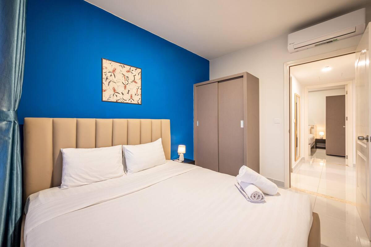 A hotel room with a large bed, a wardrobe, an air conditioning unit, and a bathroom visible through an open door.