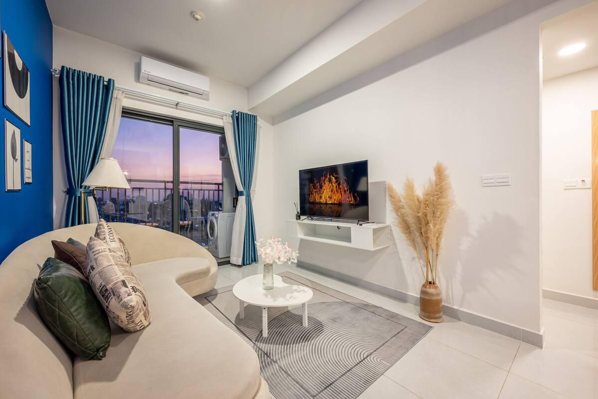 A modern living room with a sofa, a TV, a coffee table, and a view of the city.