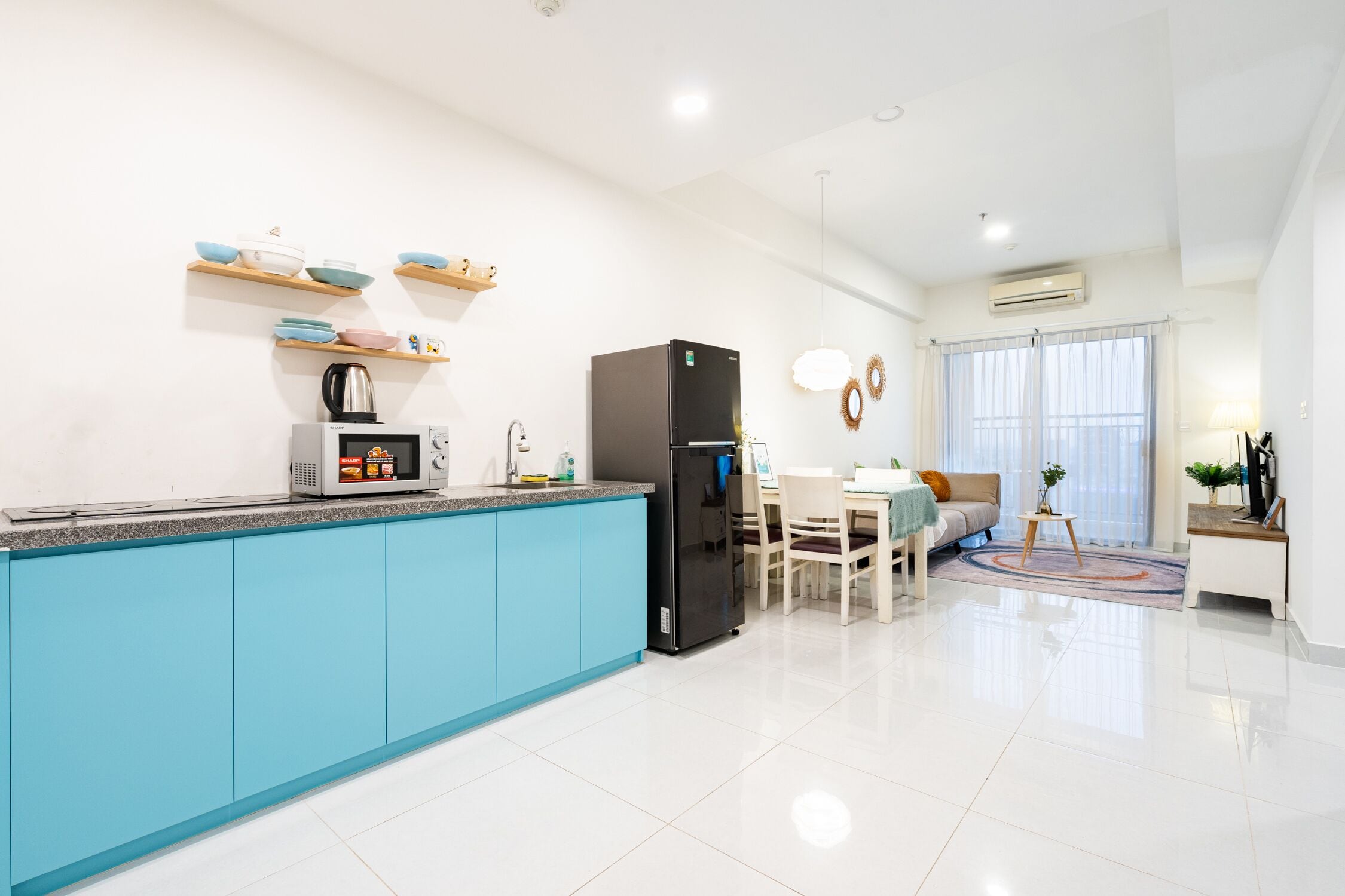 Eine moderne Küche mit blauen Schränken, einem schwarzen Kühlschrank und einer Mikrowelle. Ein Essbereich mit Tisch und Stühlen lädt zum Verweilen ein, und ein Fenster mit Vorhängen sorgt für eine gemütliche Atmosphäre.
