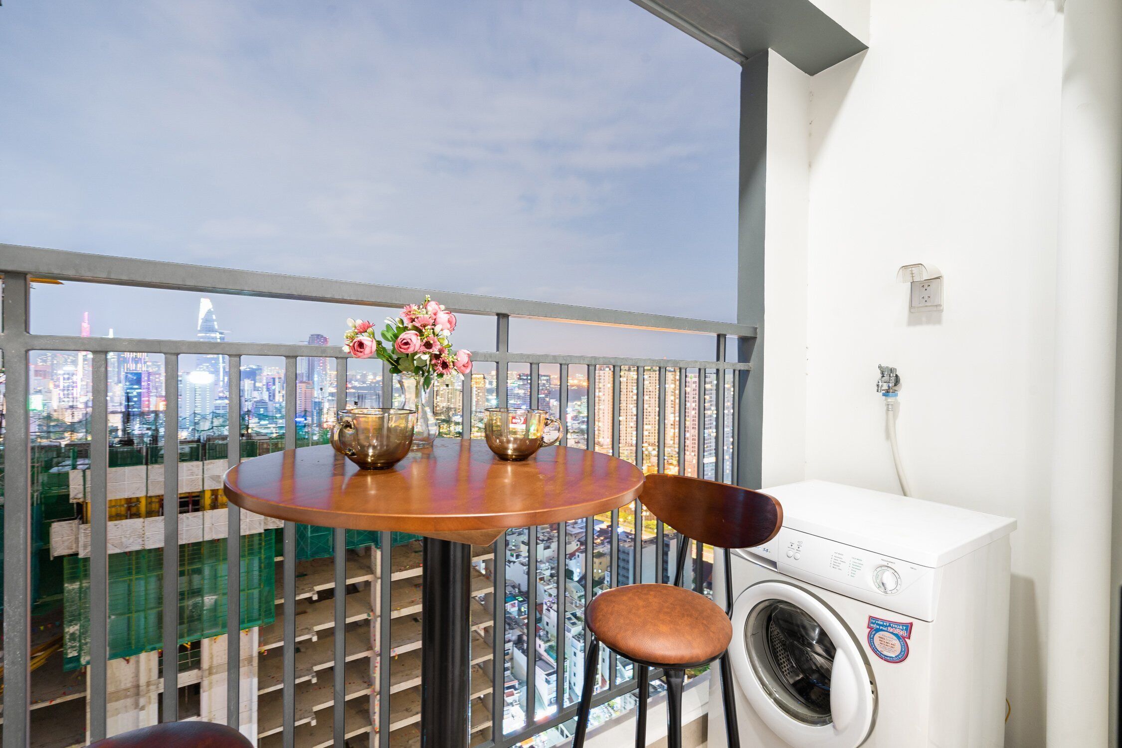 A balcony with a table, chairs, a vase of flowers, and a washing machine.