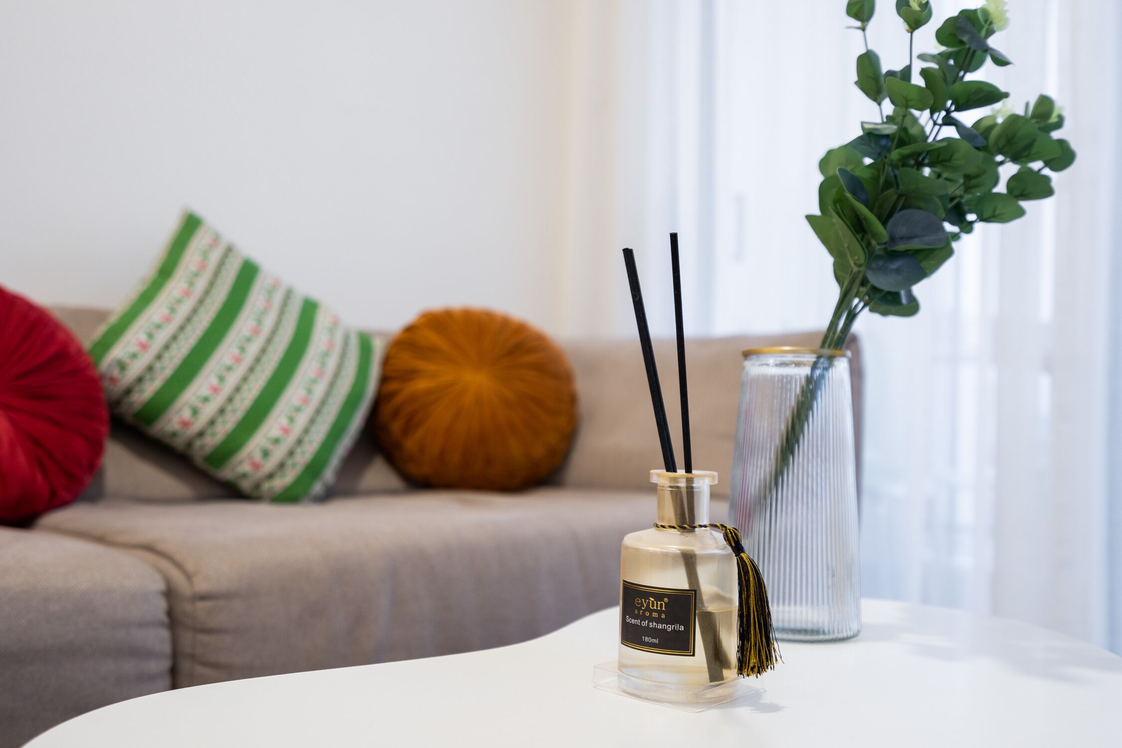 En Evyn parfume på et hvidt bord med en klar vase og en grøn plante i baggrunden.