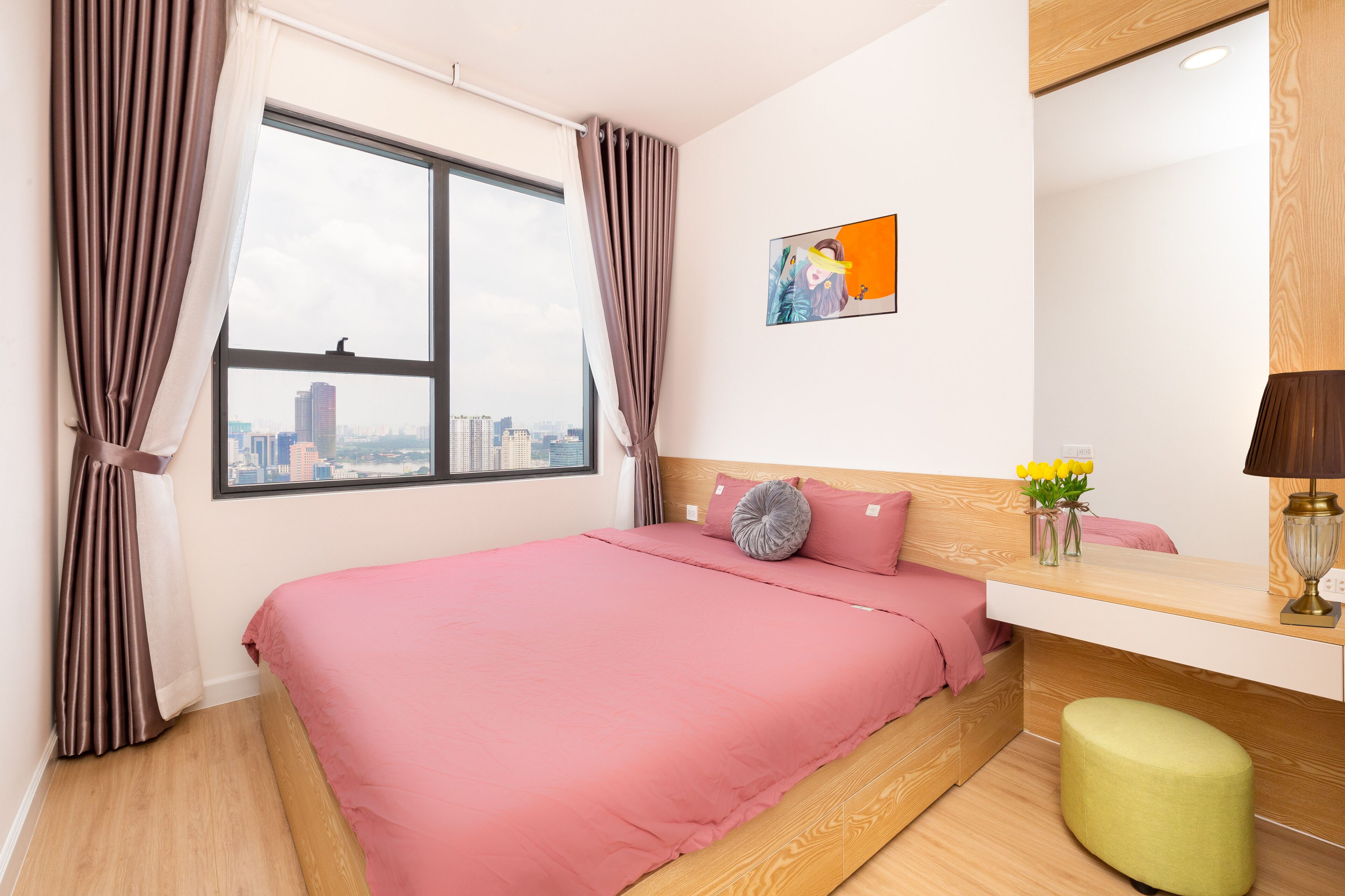 A modern bedroom with a large window, a pink bedspread, a wooden headboard, a bedside table with a lamp, and a city view.