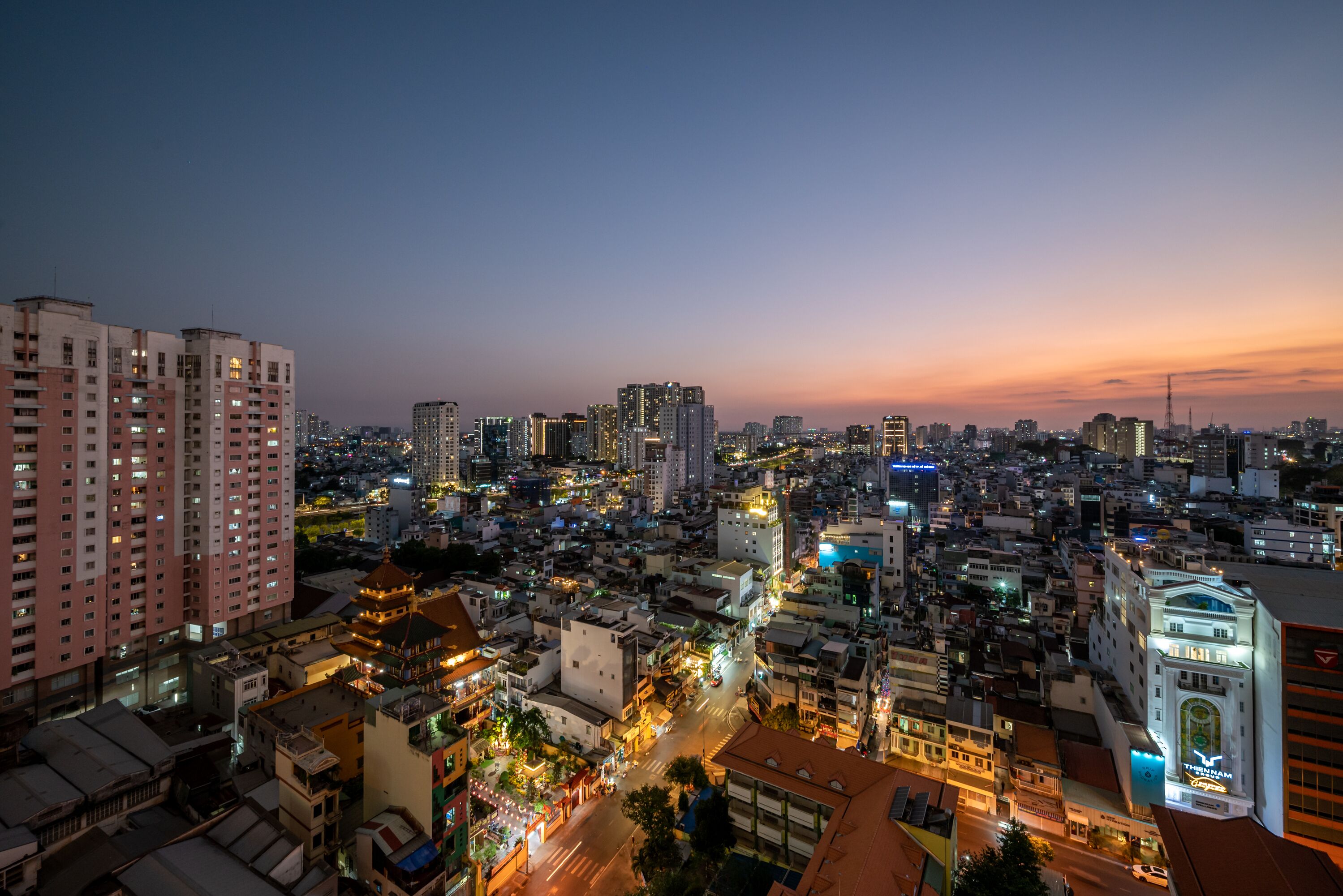 A cityscape at dusk with illuminated buildings and a prominent theater.