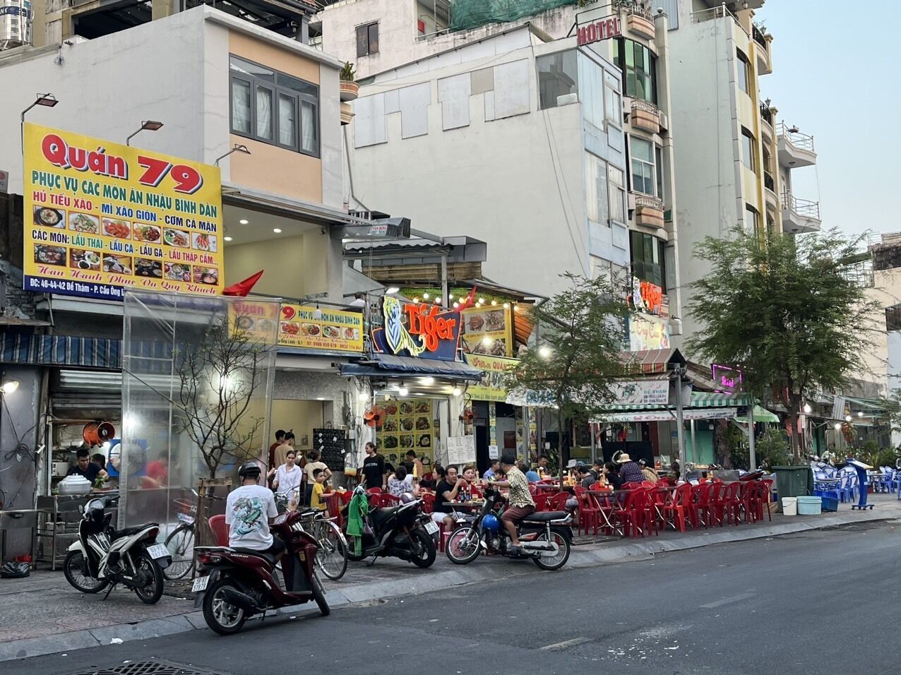 A street scene with a restaurant named 'Quán 79' and a building with a sign that reads 'HOTEL'.