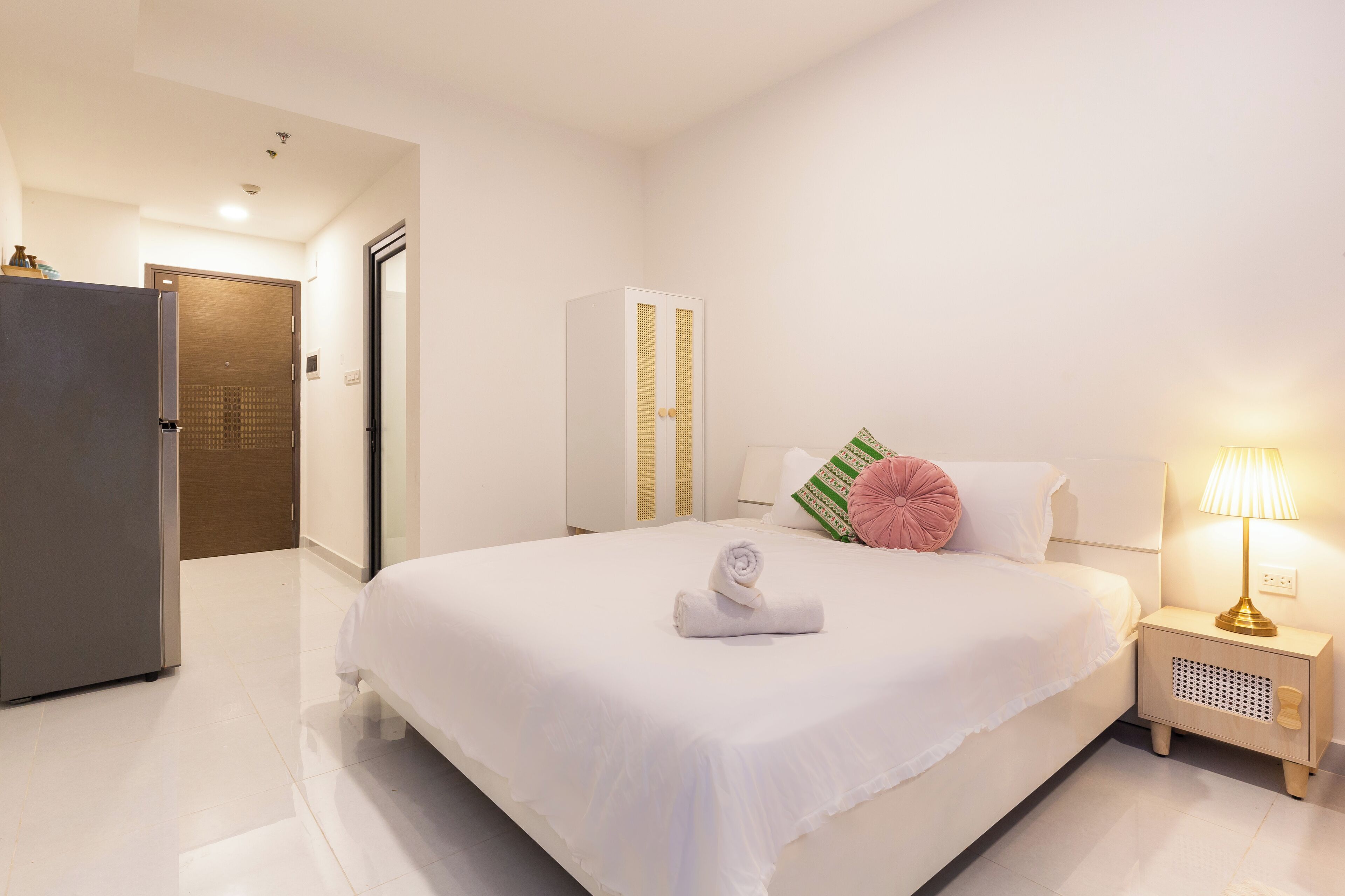 Une chambre d’hôtel avec un grand lit, une table de chevet avec une lampe, une armoire et une porte donnant sur une autre pièce.