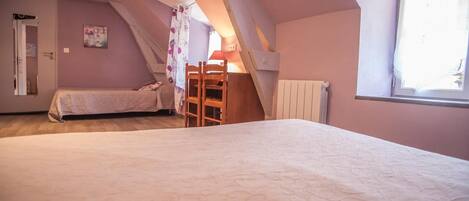 A bedroom with a sloped ceiling, a bed, a chair, and a radiator.