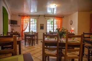 A dining area with wooden tables and chairs, orange curtains, and a clock on the wall. - Logis Auberge de L'ile (Jayac)