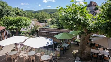 An outdoor patio with tables and chairs, surrounded by trees and overlooking a valley.