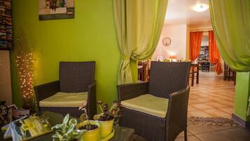 A room with wicker furniture, a dining table with potted plants, and a view into the dining area.