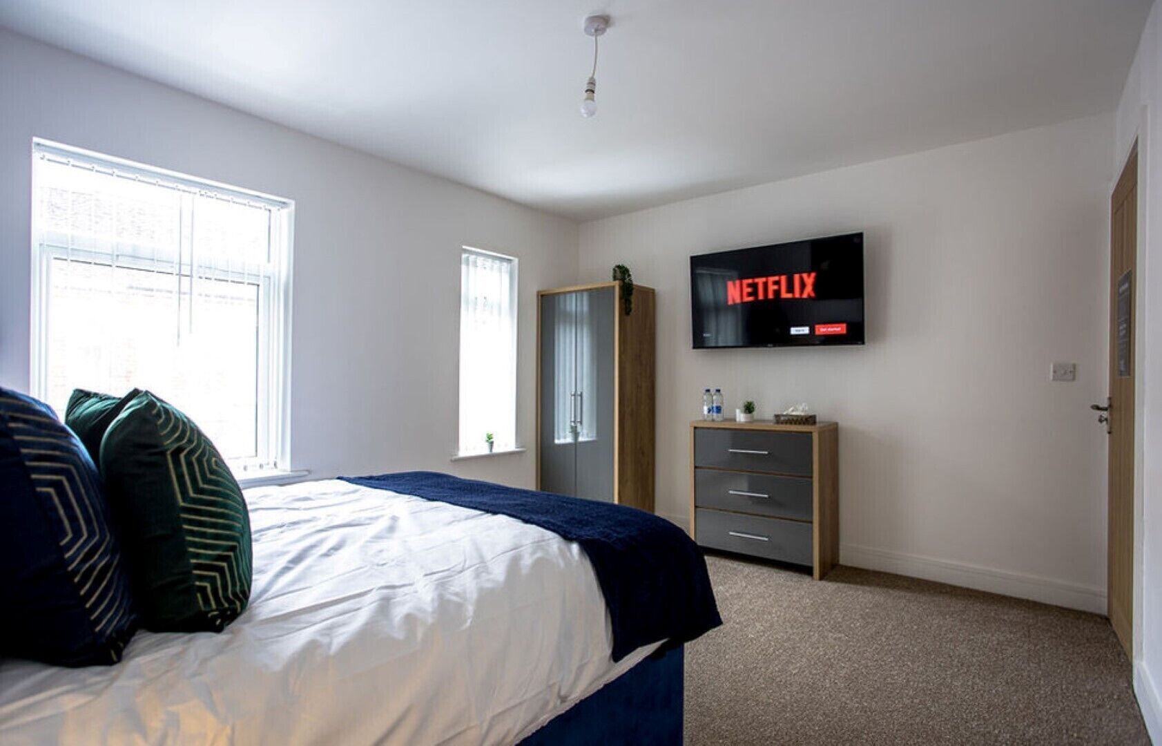 Ein Schlafzimmer mit Bett, Wandfernseher, Kleiderschrank und Fenster.