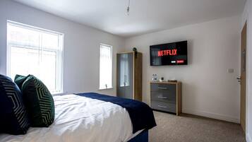 Ein Schlafzimmer mit Bett, Wandfernseher, Kleiderschrank und Fenster.
