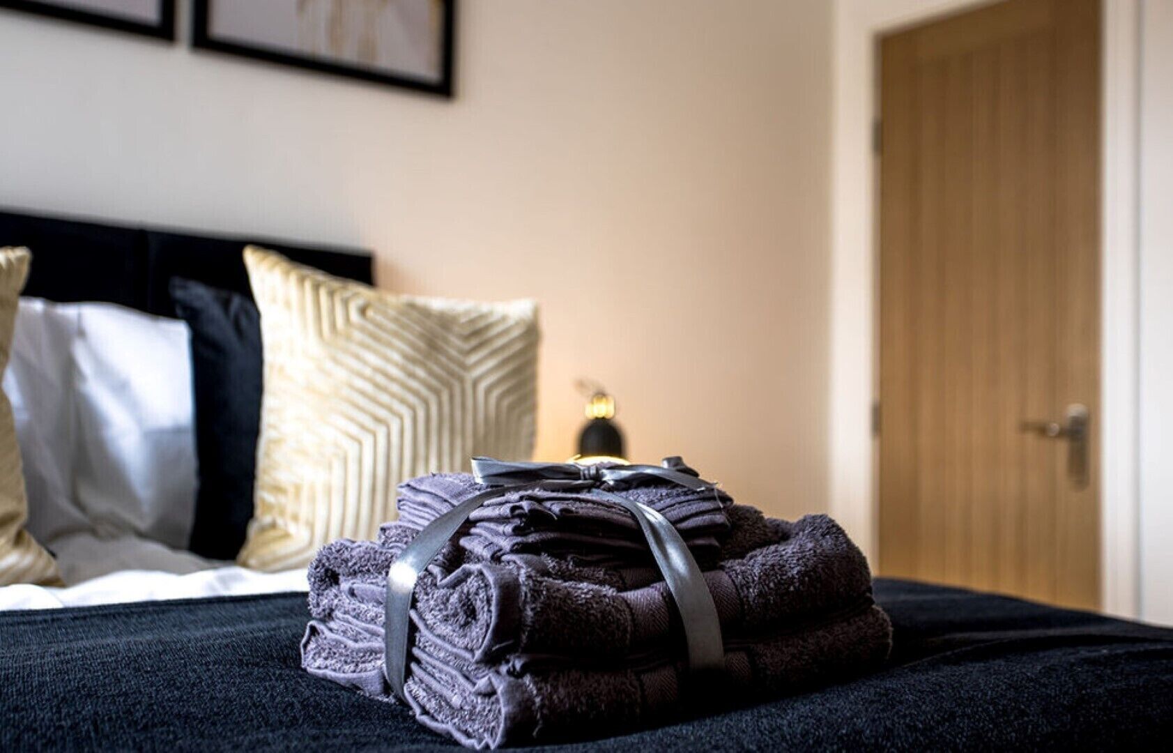 A neatly made bed with a black bedspread and a folded towel on top.