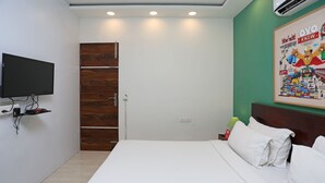 Une chambre d’hôtel avec un lit, un téléviseur fixé au mur, une armoire en bois, une affiche accrochée au mur et une table de chevet avec une lampe.