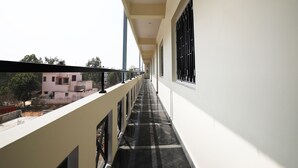 Un couloir avec un balcon d’un côté, offrant une vue sur des immeubles et des arbres.