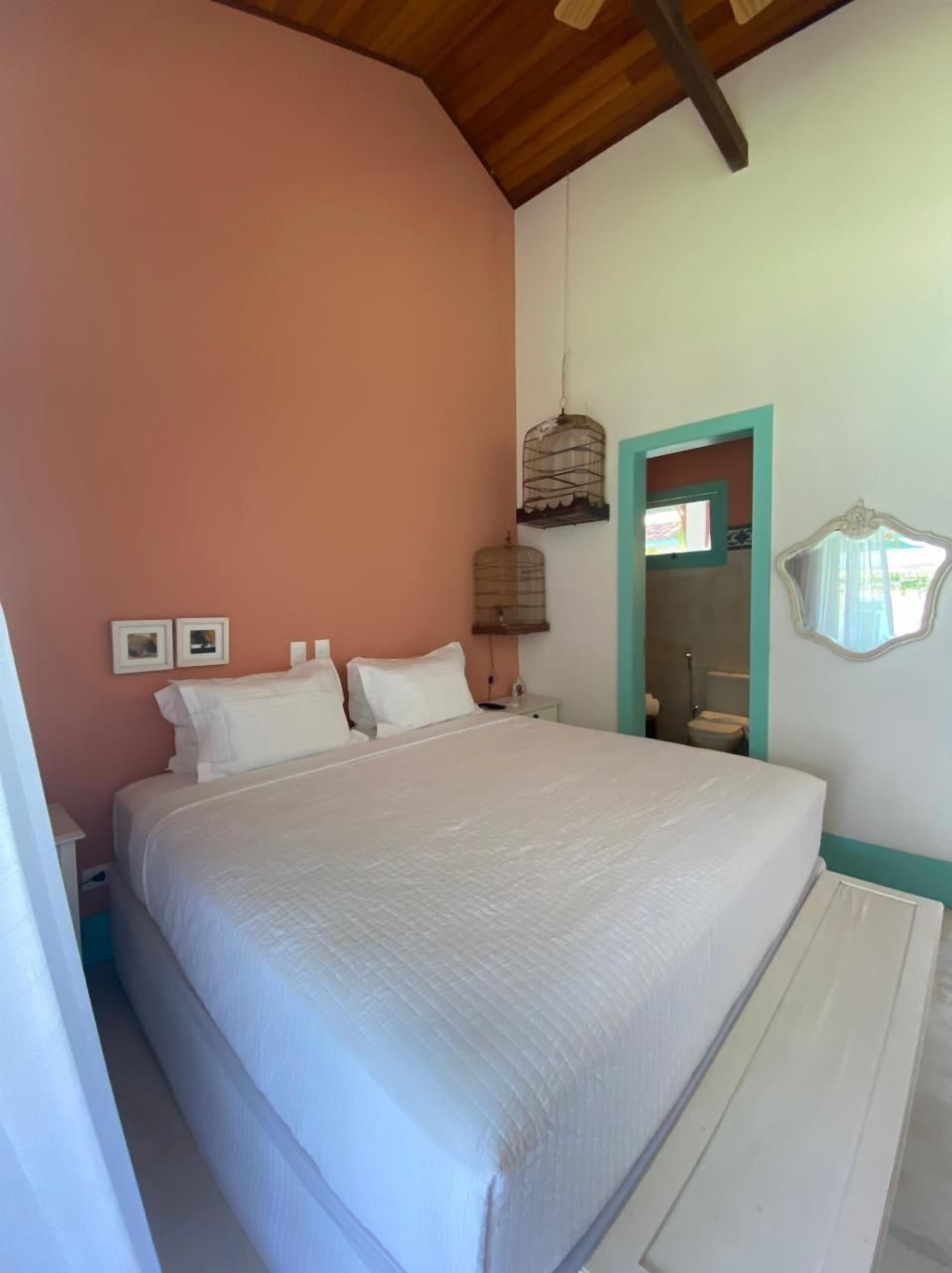 A bedroom with a large bed, a wooden ceiling, a birdcage, and a bathroom visible through an open door.