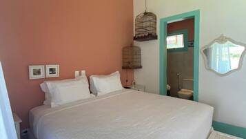 A bedroom with a large bed, a wooden ceiling, a birdcage, and a bathroom visible through an open door.