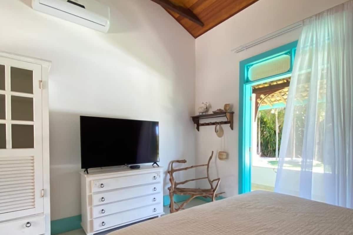 Une chambre à coucher avec un lit, une télévision, une armoire et une fenêtre avec des rideaux.