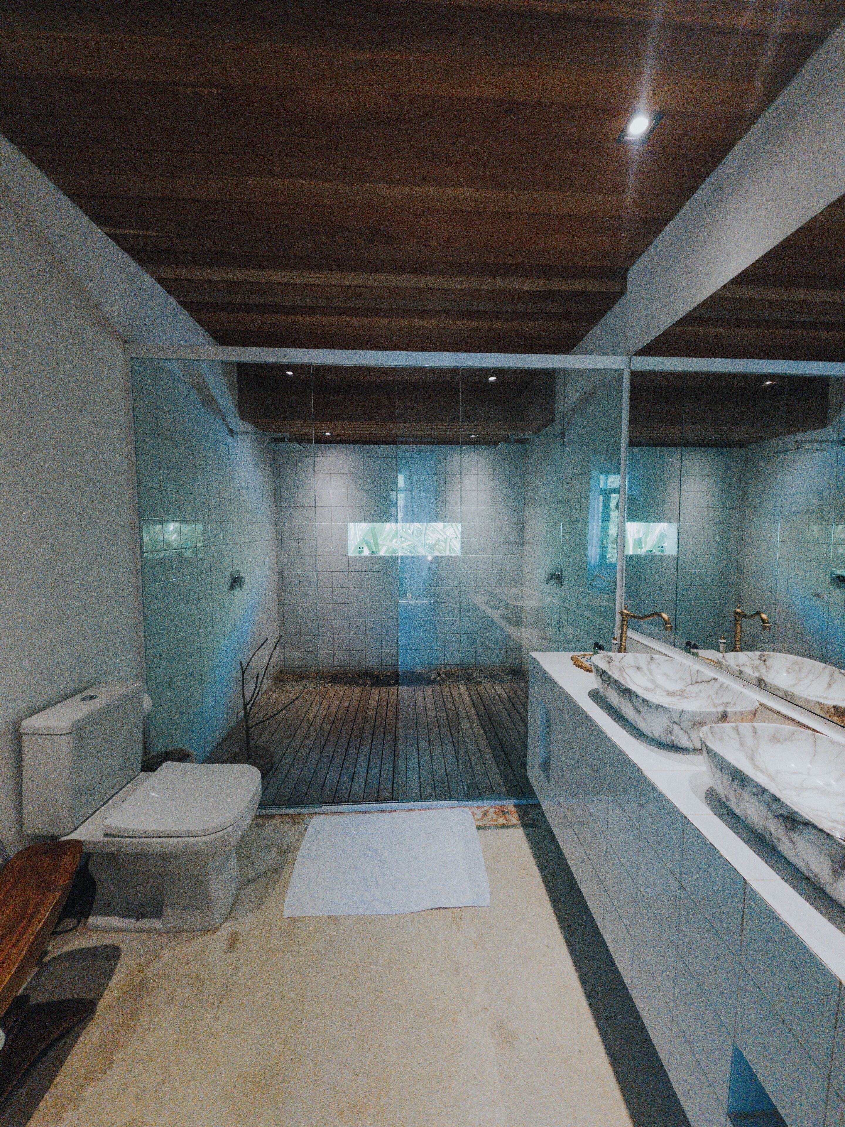 Une salle de bain avec un plancher en bois, des toilettes, un lavabo avec un receveur en marbre et un grand miroir.