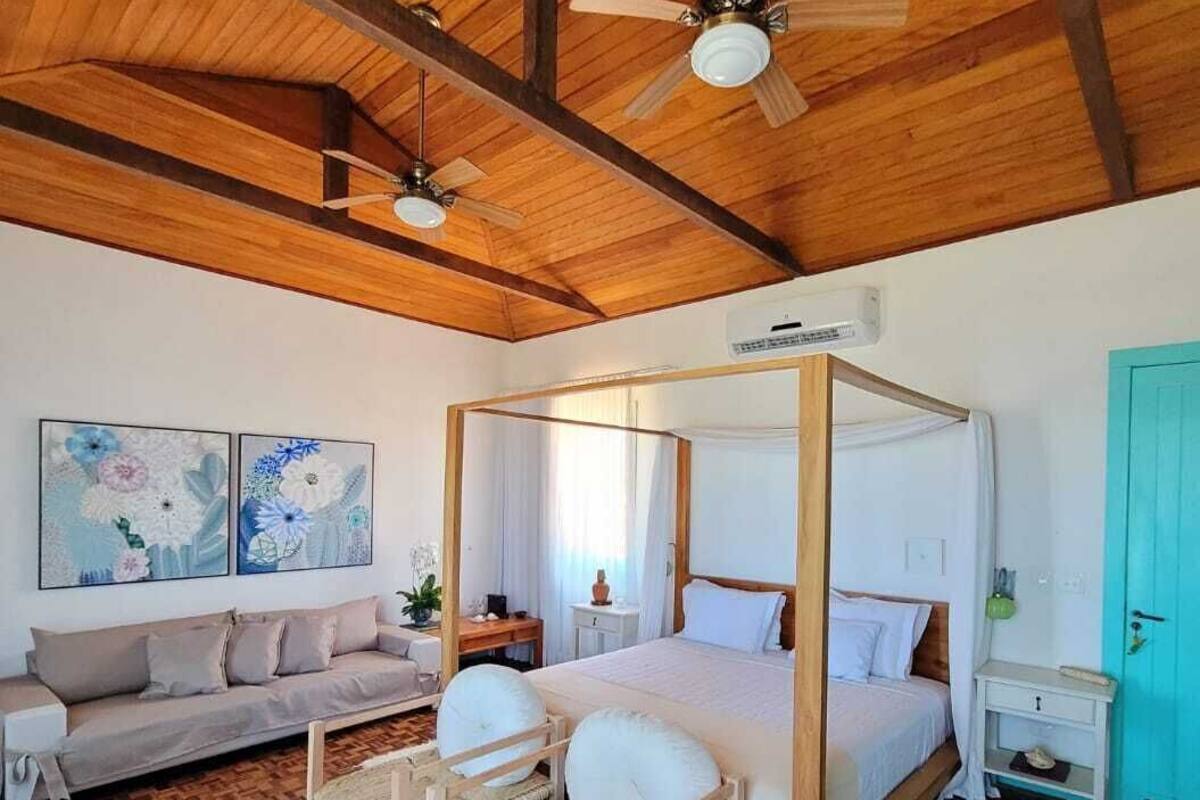 Une chambre à coucher avec un lit à baldaquin, un ventilateur de plafond, un plancher en bois, un canapé et des œuvres d’art accrochées au mur.
