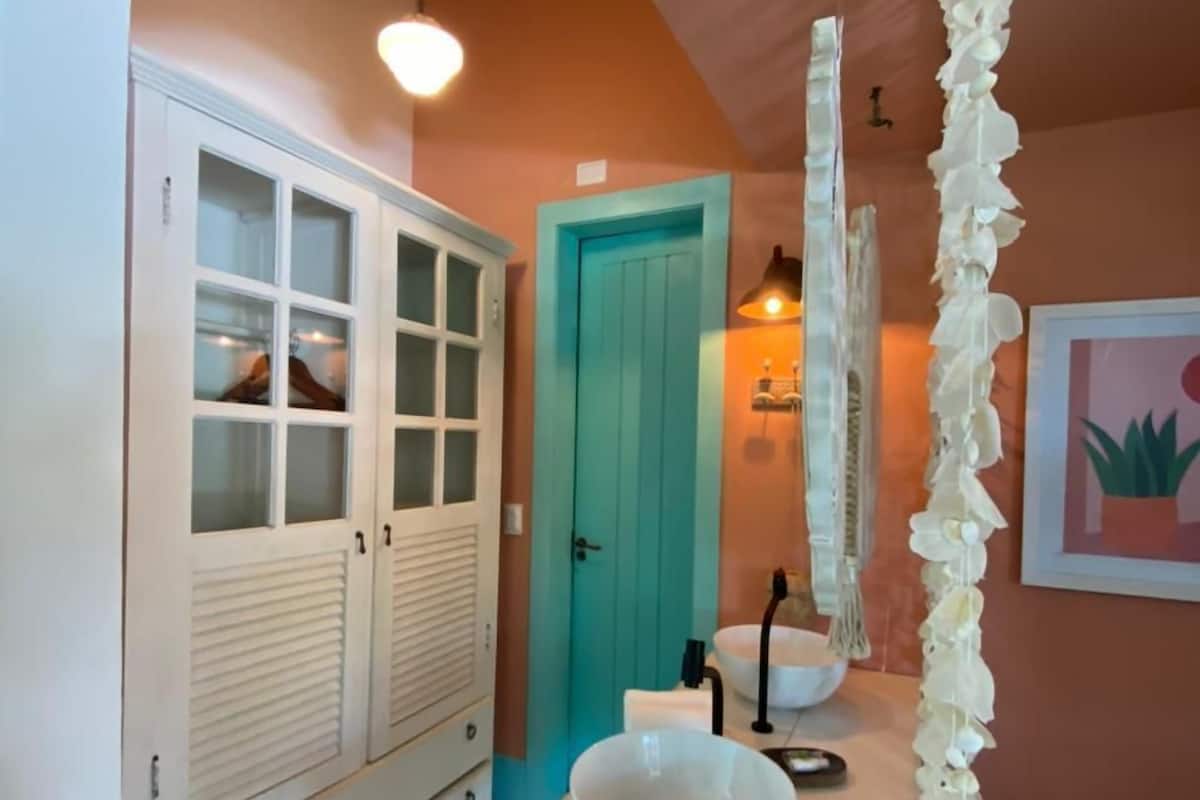 Une salle de bain avec un meuble-lavabo blanc, une porte turquoise, un lavabo blanc et un luminaire suspendu.