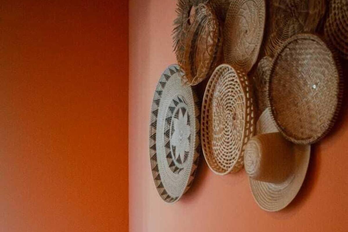Un lit avec une literie blanche et un mur décoré de paniers et de chapeaux tressés.