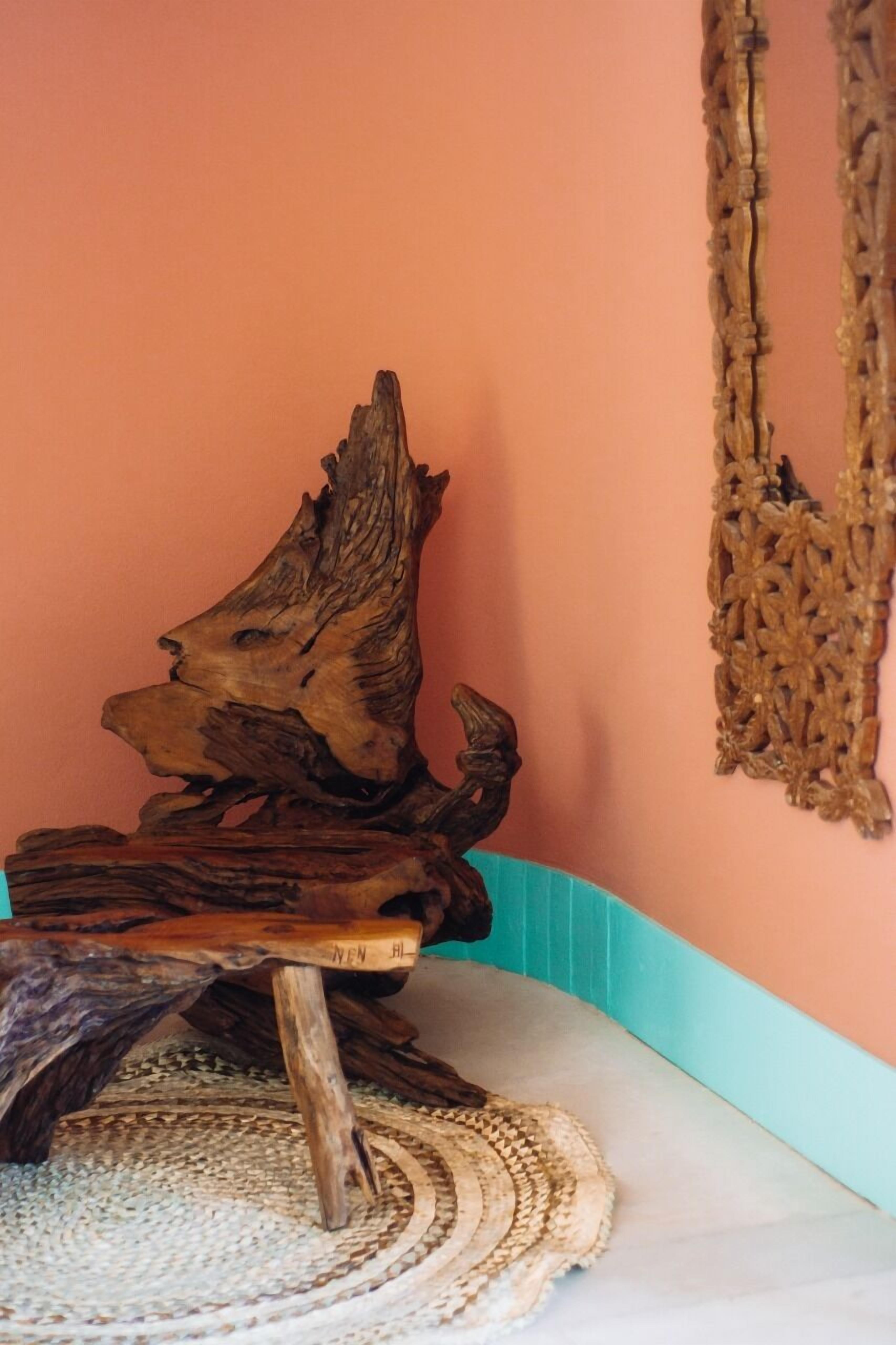 A piece of driftwood art on a white surface with a woven mat underneath, against a peach-colored wall with a blue trim.
