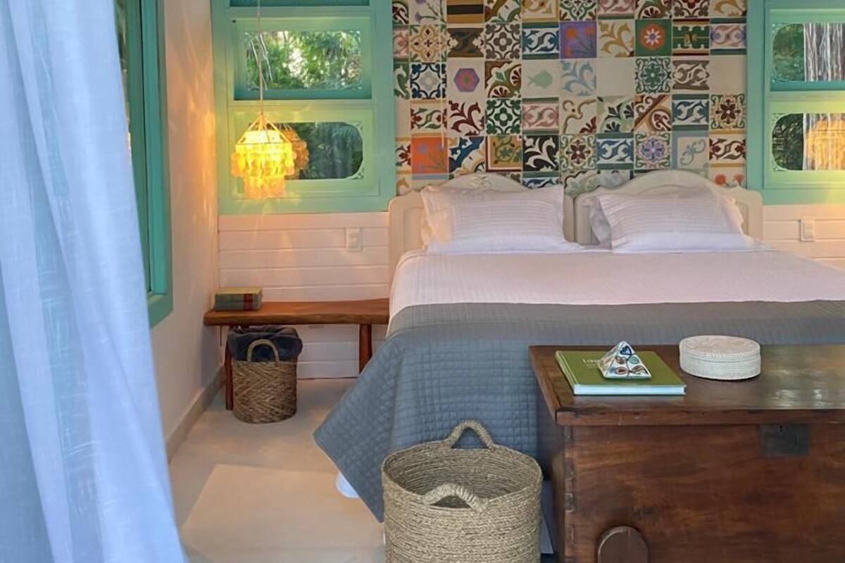 Une chambre à coucher avec un lit, une table de chevet en bois, un panier en osier et un luminaire suspendu.