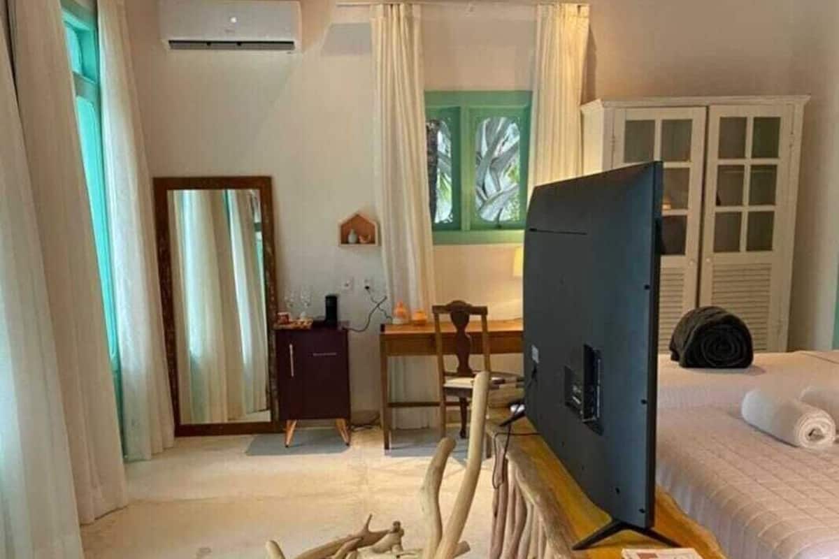 Une pièce avec un plafond en bois, un téléviseur posé sur un meuble en bois, un lit, un bureau avec une chaise et une fenêtre avec des rideaux.